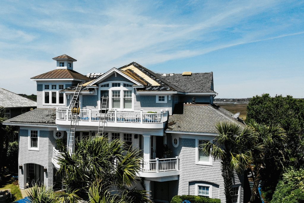 A large blue coastal home part-way through a roof replacement.