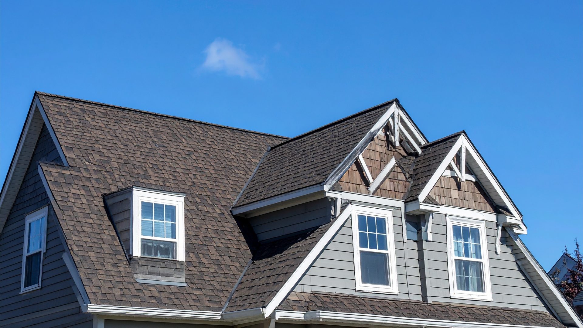 Dormers and shingle detail on a residential roof against a clear sky.